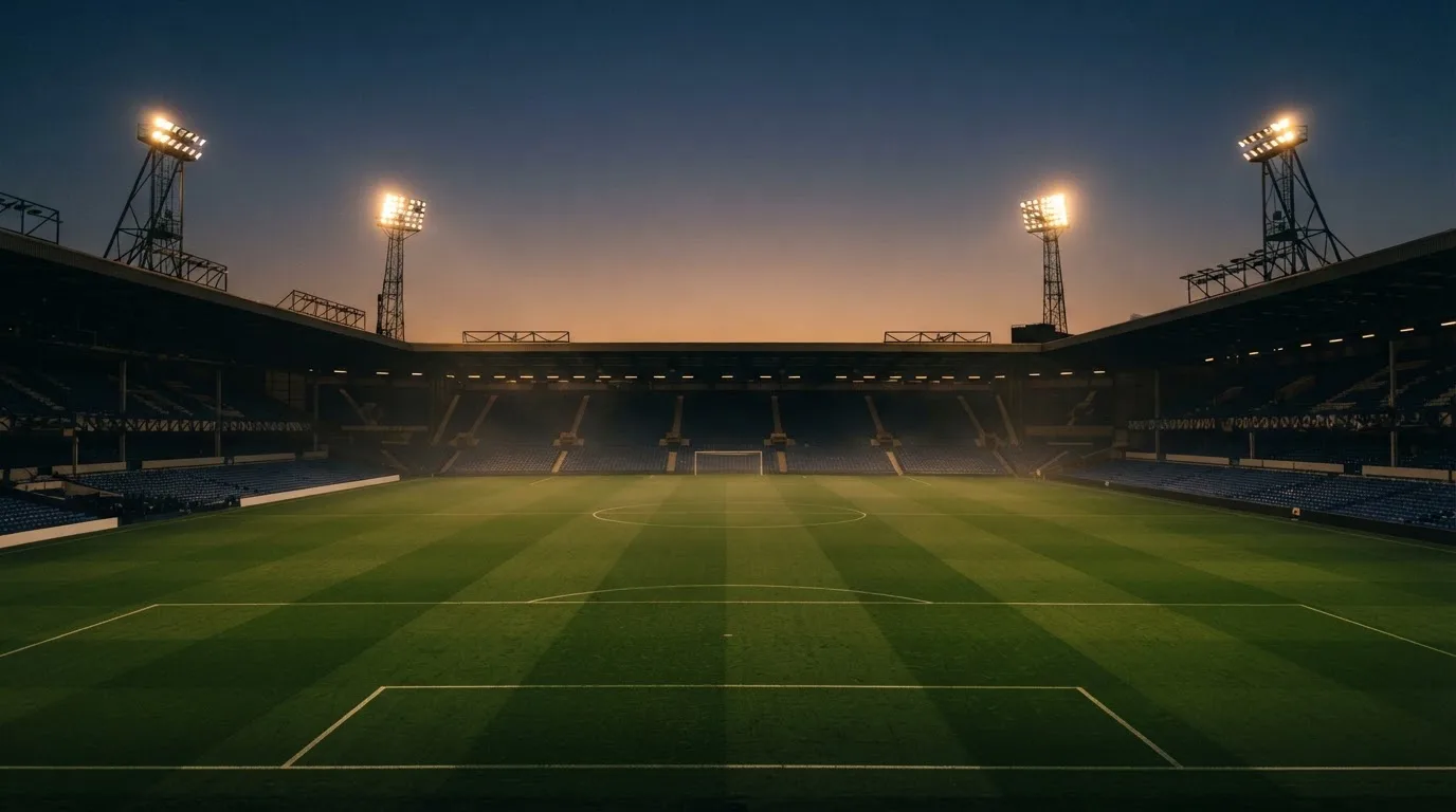 An empty football stadium with floodlight masts at dusk