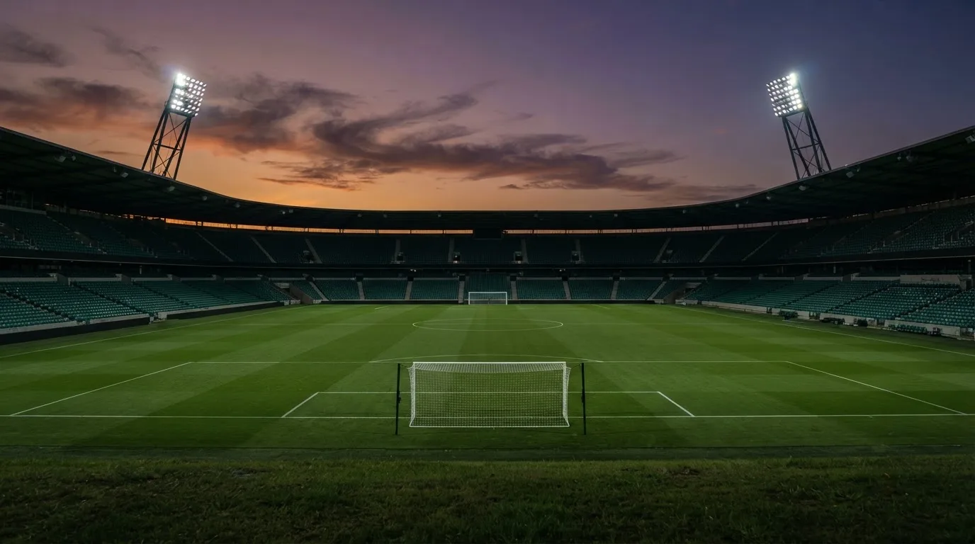 An empty football stadium with floodlight masts at dusk
