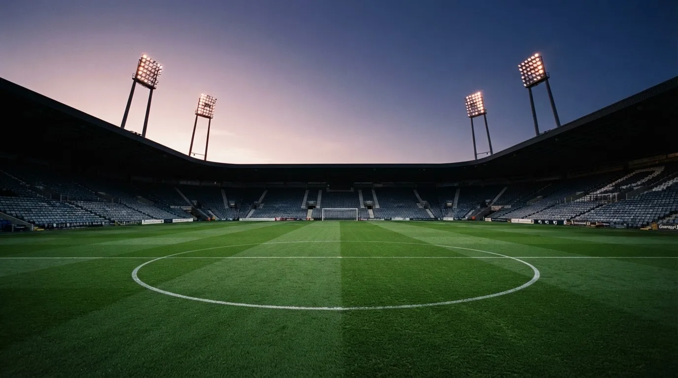 An empty football stadium with floodlight masts at dusk