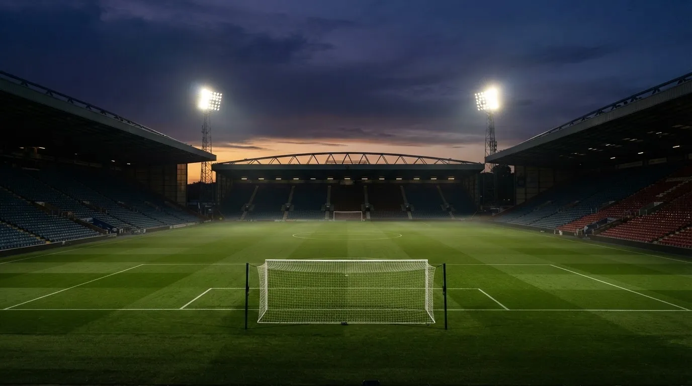 An empty football stadium with floodlight masts at dusk