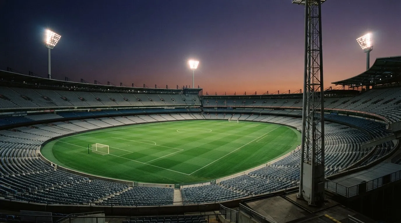 An empty football stadium with floodlight masts at dusk