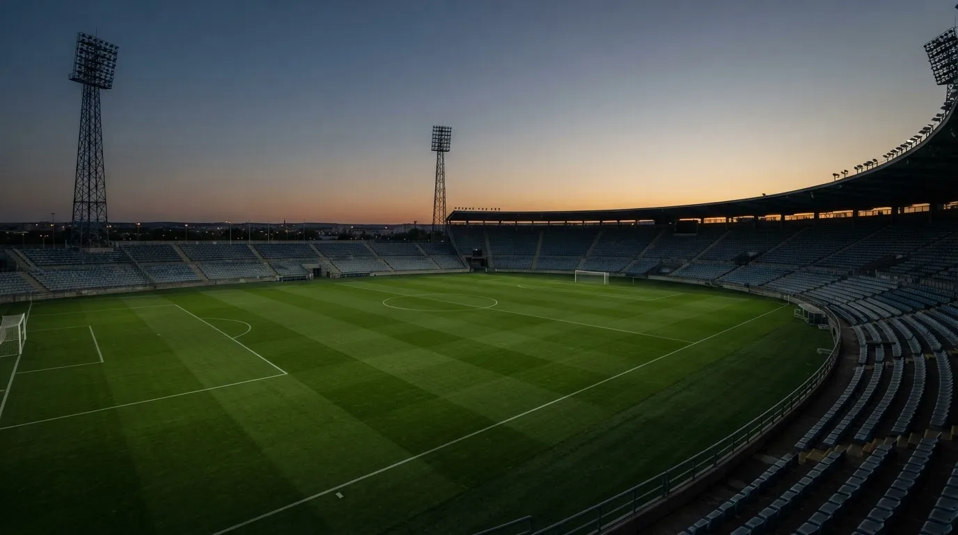 An empty football stadium with floodlight masts at dusk